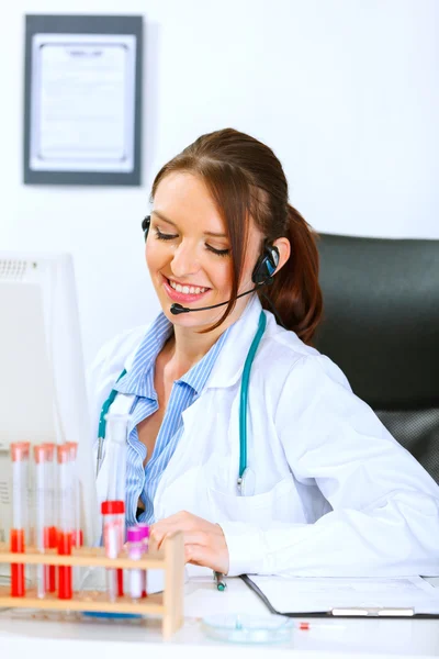 Mujer doctora sonriente con auriculares sentados en la mesa de la oficina y ta — Foto de Stock