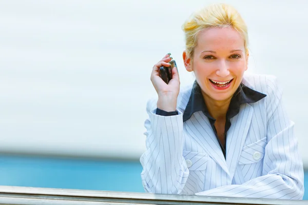 Glimlachende zakenvrouw met mobile in de hand leunend op reling op office bui — Stockfoto