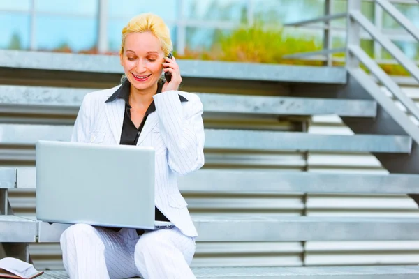 Lächelnde Geschäftsfrau, die auf der Treppe sitzt und über Handy und Internet spricht — Stockfoto