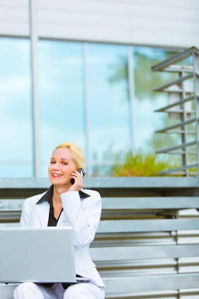 Mujer de negocios sonriente con portátil sentado en las escaleras en el edificio de oficinas y — Foto de Stock