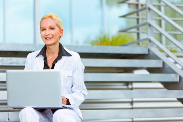 Lächelnde Geschäftsfrau sitzt im Bürogebäude auf der Treppe und benutzt Lapto — Stockfoto
