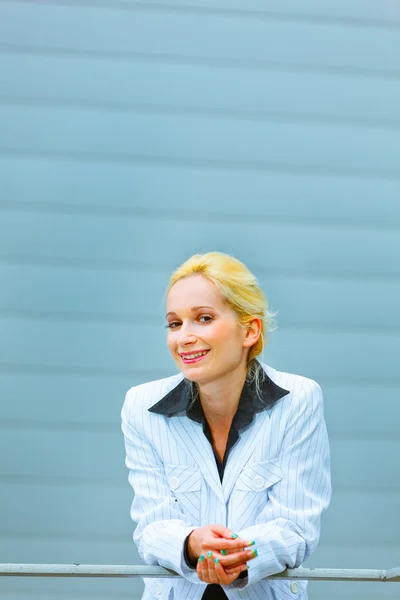 Sorrindo mulher de negócios apoiando-se em trilhos no prédio de escritórios — Fotografia de Stock