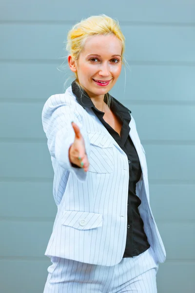Standing at office building smiling business woman stretches out hand — Stock Photo, Image