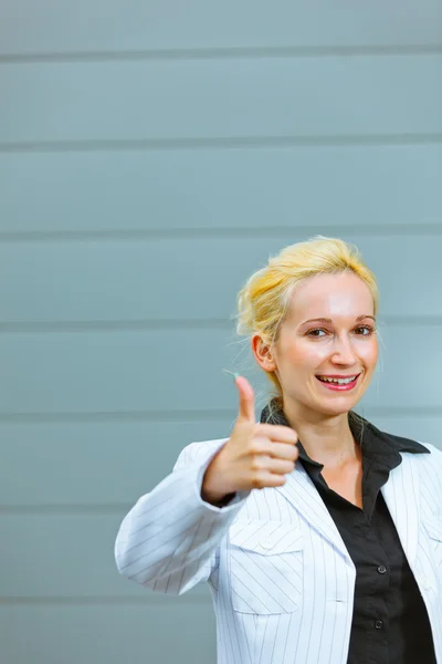 Standing at office building smiling business woman showing thumbs up gestur — Stock Photo, Image