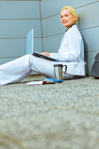 Sonriente mujer de negocios moderna en el piso en el edificio de oficinas trabajando en el ordenador portátil — Foto de Stock