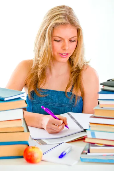 Девушка сидит за столом с большим количеством книг и делает домашнее задание — стоковое фото