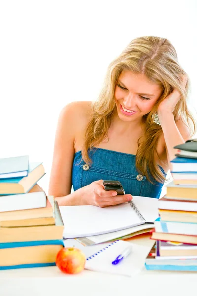 Улыбающаяся девочка читает смс на мобильном вместо того, чтобы делать домашнее задание — стоковое фото