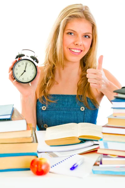 Smiling teengirl with alarm clock sitting at table — Stock Photo, Image