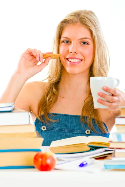 Χαμογελώντας teengirl κάθεται σε τραπέζι με βιβλία και πίνοντας τσάι με cookie — Φωτογραφία Αρχείου
