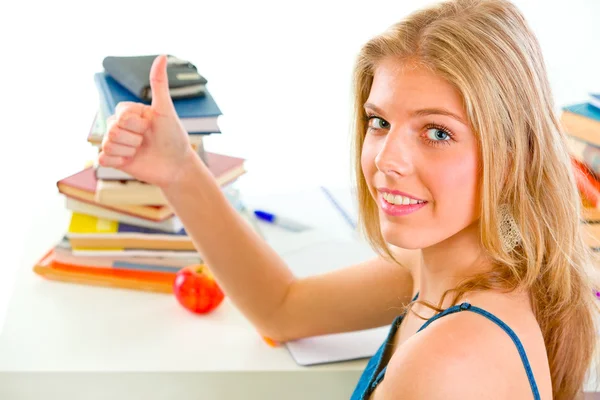 Smiling teen girl sitting at table with books and showing thumbs — Stock Photo, Image