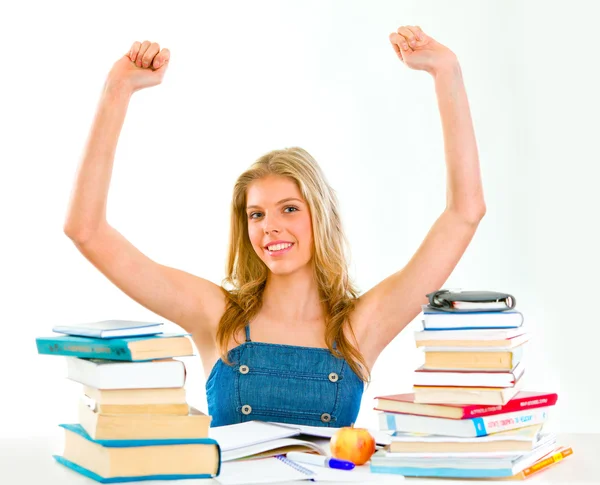 Pleased young girl with raised hands sitting at desk with books — Stock Photo, Image