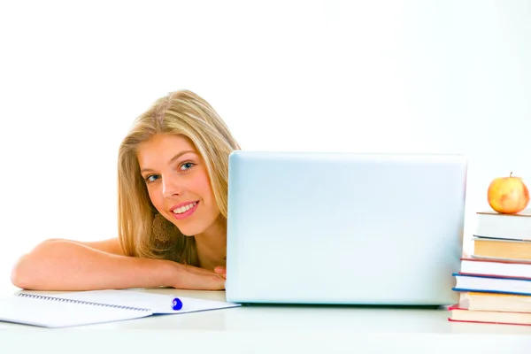 Сидя за столом, улыбаясь девочка-подросток смотрит из ноутбука — стоковое фото