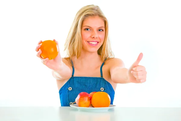 Smiling pretty girl giving orange and showing thumbs up — Stock Photo, Image