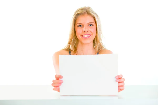 Lovely girl sitting at table and holding blank paper — Stock Photo, Image