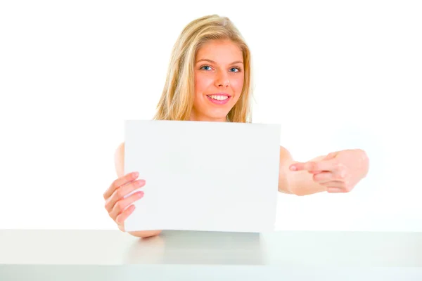 Chica sonriente sentada en la mesa y señalando en papel en blanco —  Fotos de Stock