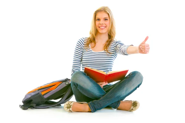 Duimschroef opwaarts gebaar glimlachend jong meisje met Schooltasje en boek sittin weergegeven: — Stockfoto