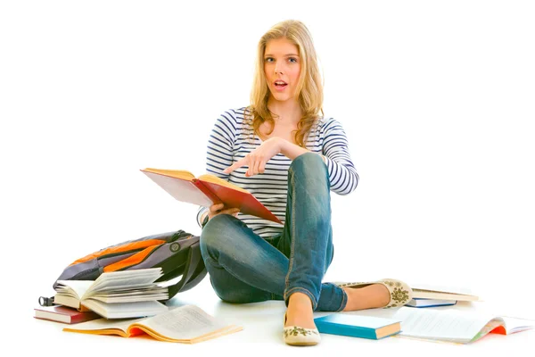 Shocked teen girl sitting on floor with schoolbag and pointing finger in op — Stock Photo, Image