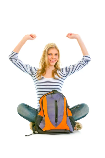 Задоволена дівчина сидить на підлозі зі шкільною сумкою і радіє її успіху — стокове фото