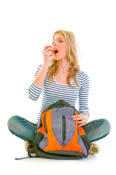 Красива дівчина сидить на підлозі зі шкільною сумкою і їсть яблуко — стокове фото