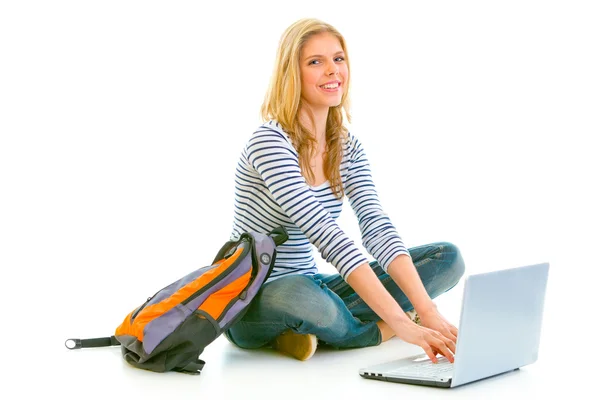 Uśmiechający się teengirl siedzi na podłodze z tornister i korzysta z laptopa — Zdjęcie stockowe