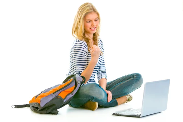 Pleased teengirl sitting on floor with schoolbag and laptop — Stock Photo, Image