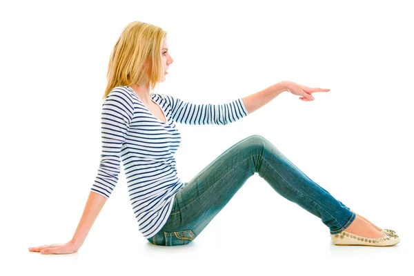Bella ragazza adolescente seduta sul pavimento e che punta il dito contro lo spazio copia — Foto Stock