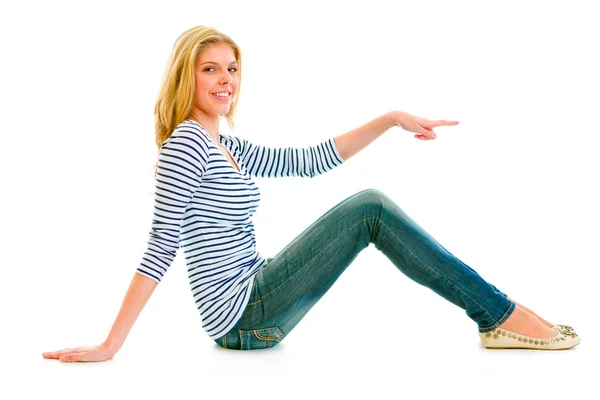 Smiling beautiful teen girl sitting on floor and pointing finger at somethi — Stock Photo, Image