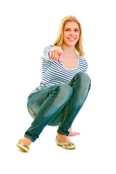 Smiling beautiful teen girl squatting and pointing finger at you — Stock Photo, Image