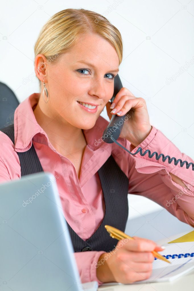 Smiling business woman sitting at office desk and talking on phone
