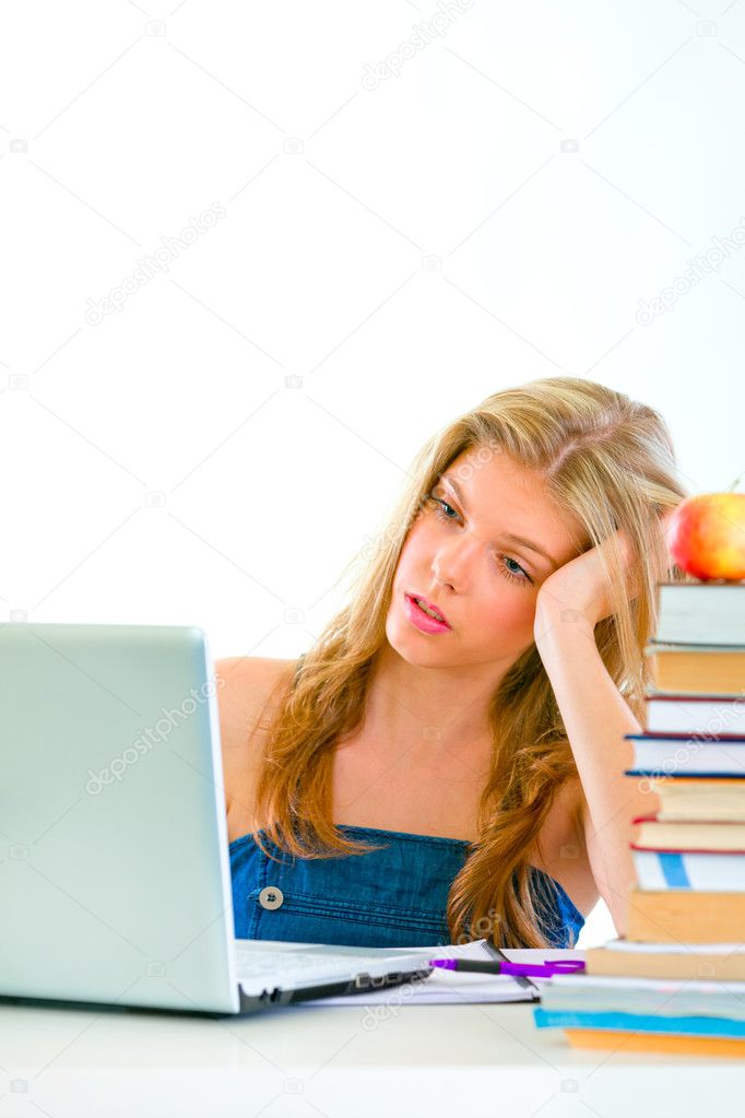 Bored teen girl sitting at table and looking on laptop