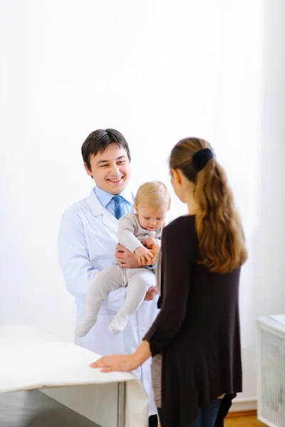 Dětský doktor drží dítě a mluví s matkou — Stock fotografie