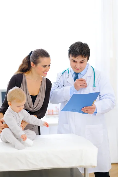 Pediatrische arts praten met moeder terwijl baby zittend op tafel — Stockfoto