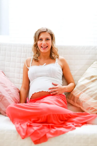 Usmívající se těhotná žena sedící na gauči — Stock fotografie