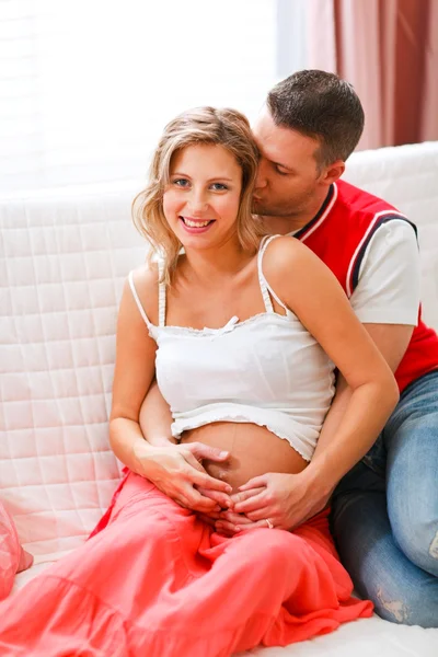 Молодой муж обнимает свою счастливую беременную жену и целует ее — стоковое фото