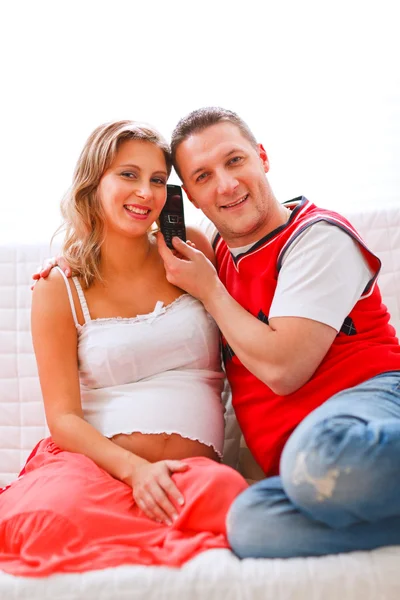 Mujer embarazada sonriente sentada con su marido en el sofá y hablando — Foto de Stock