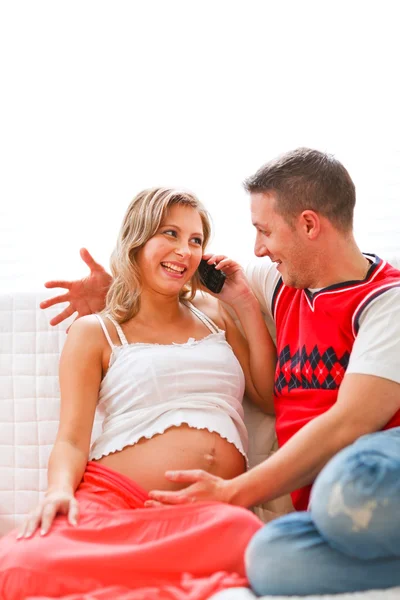 Молодая беременная женщина сидит с мужем на диване и говорит — стоковое фото