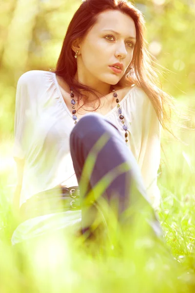 Nachdenkliches hübsches Mädchen sitzt auf grünem Gras — Stockfoto
