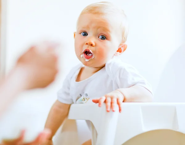Comer untado adorable bebé en silla de bebé alimentación por la madre —  Fotos de Stock