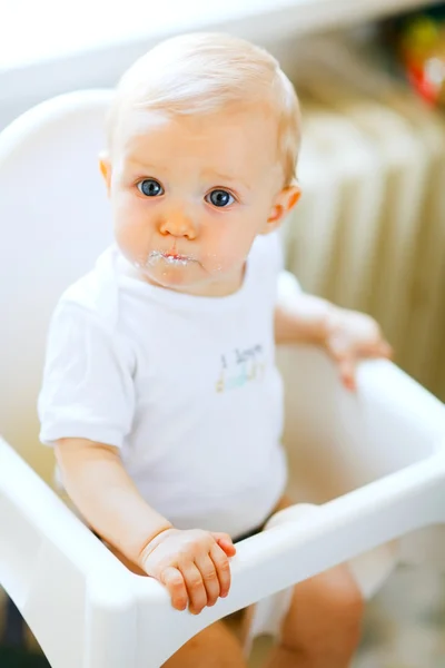 Eat smeared lovely baby in baby chair impressively looking — Stock Photo, Image