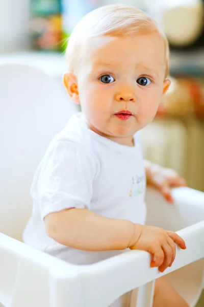 Eat smeared pretty baby in baby chair interestedly looking — Stock Photo, Image