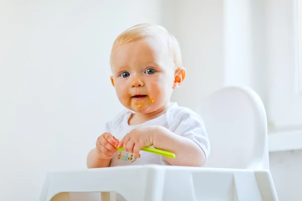 Comer manchado lindo bebê com colher na mão — Fotografia de Stock