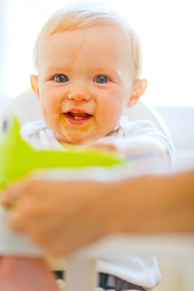 Eat smeared smiling baby girl sitting in baby chair — Stock Photo, Image