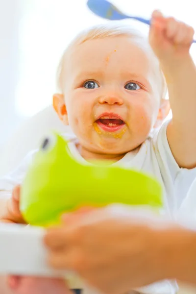 在婴儿椅玩勺子吃被涂污的可爱宝贝女孩 — 图库照片