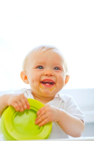 Comer manchado sorrindo bebê menina brincando com prato — Fotografia de Stock