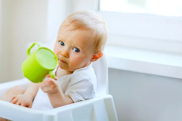 Schattige babymeisje, zittend in de stoel en houden baby cup — Stockfoto