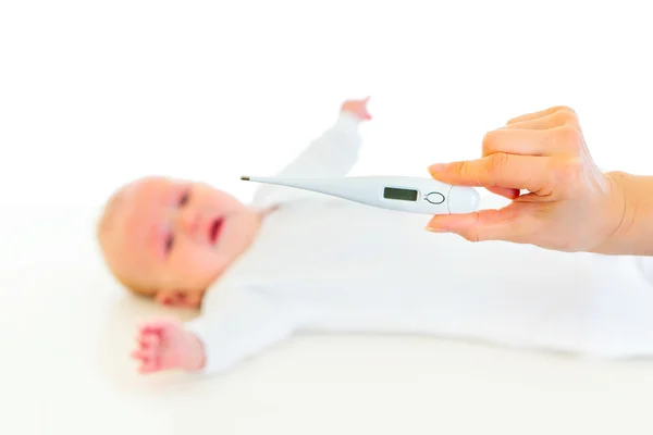 Womans hand holding medical thermometer and crying baby laying on back in — Stock Photo, Image