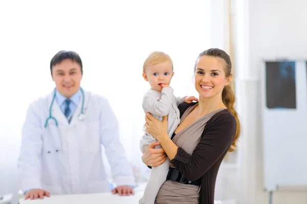 Mother holding adorable baby and doctor in background Stock Photo