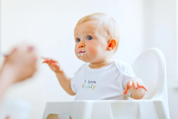Comer untado precioso bebé en silla de bebé alimentación por la madre Imagen de archivo