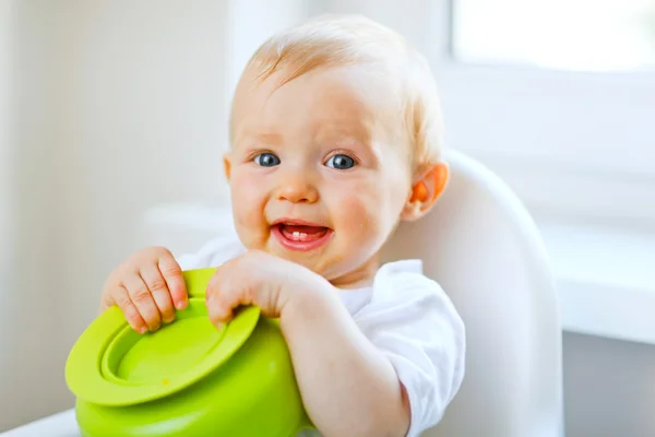 Adorable baby girl sitting in baby chair and playing with plate Royalty Free Stock Photos