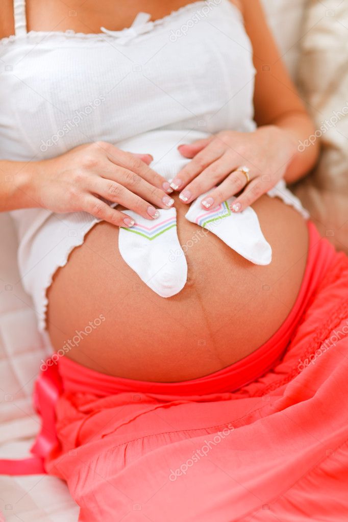 Closeup on pregnant woman belly with baby's socks on it